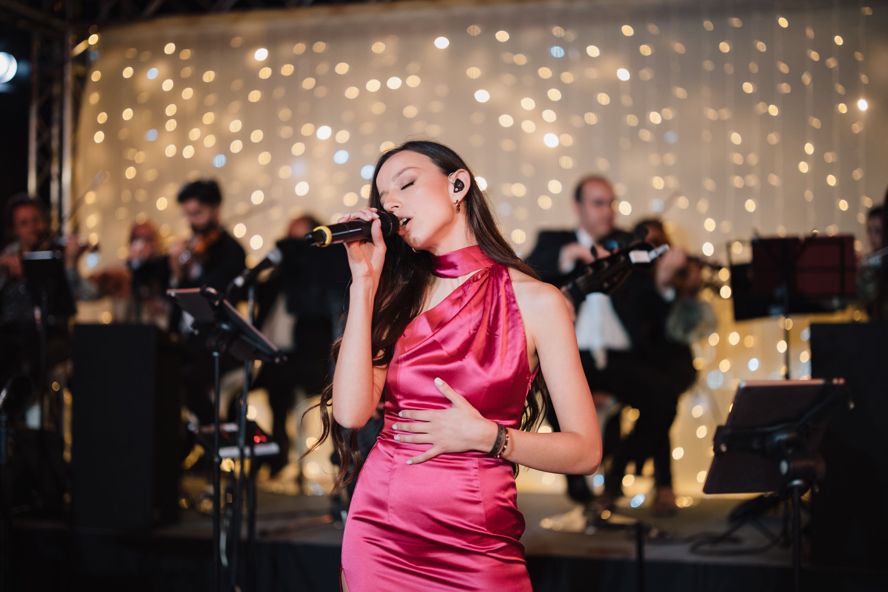 Violinists in a pop orchestra with a fairylight curtain backdrop.