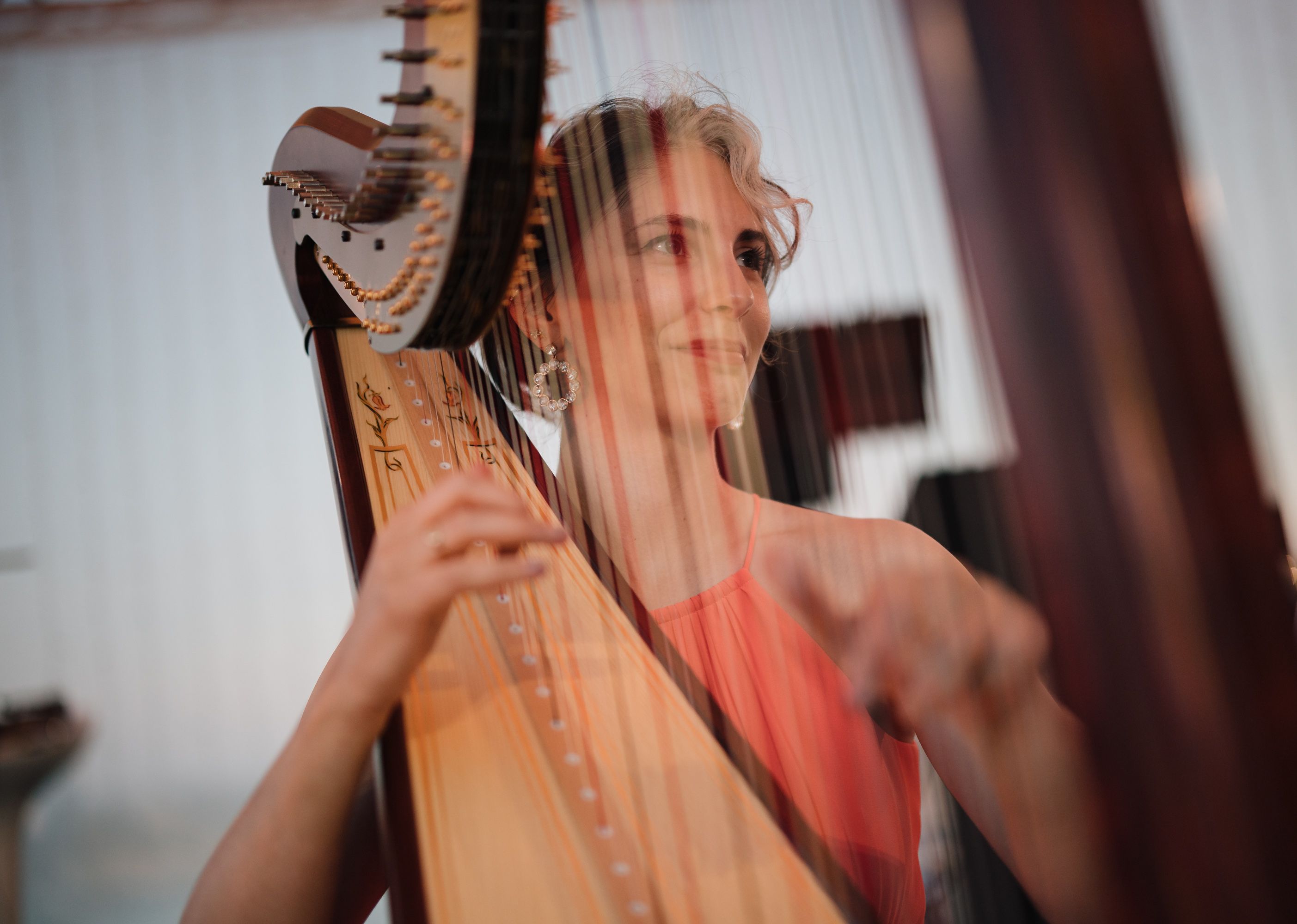 Female harpist smiling through the strings of her harp