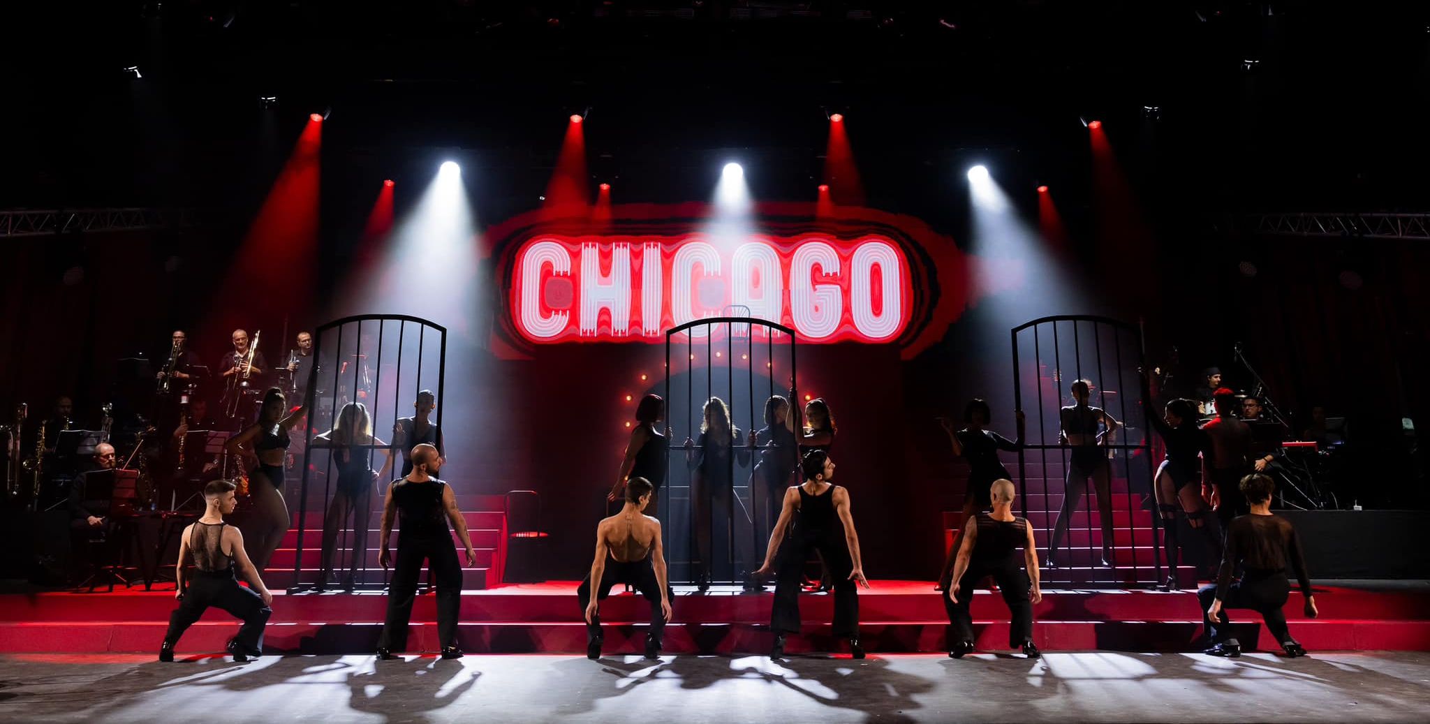 A musical theatre setup with various spotlights, two staircases, musicians on either side and a large team of dancers in a final position on the large stage