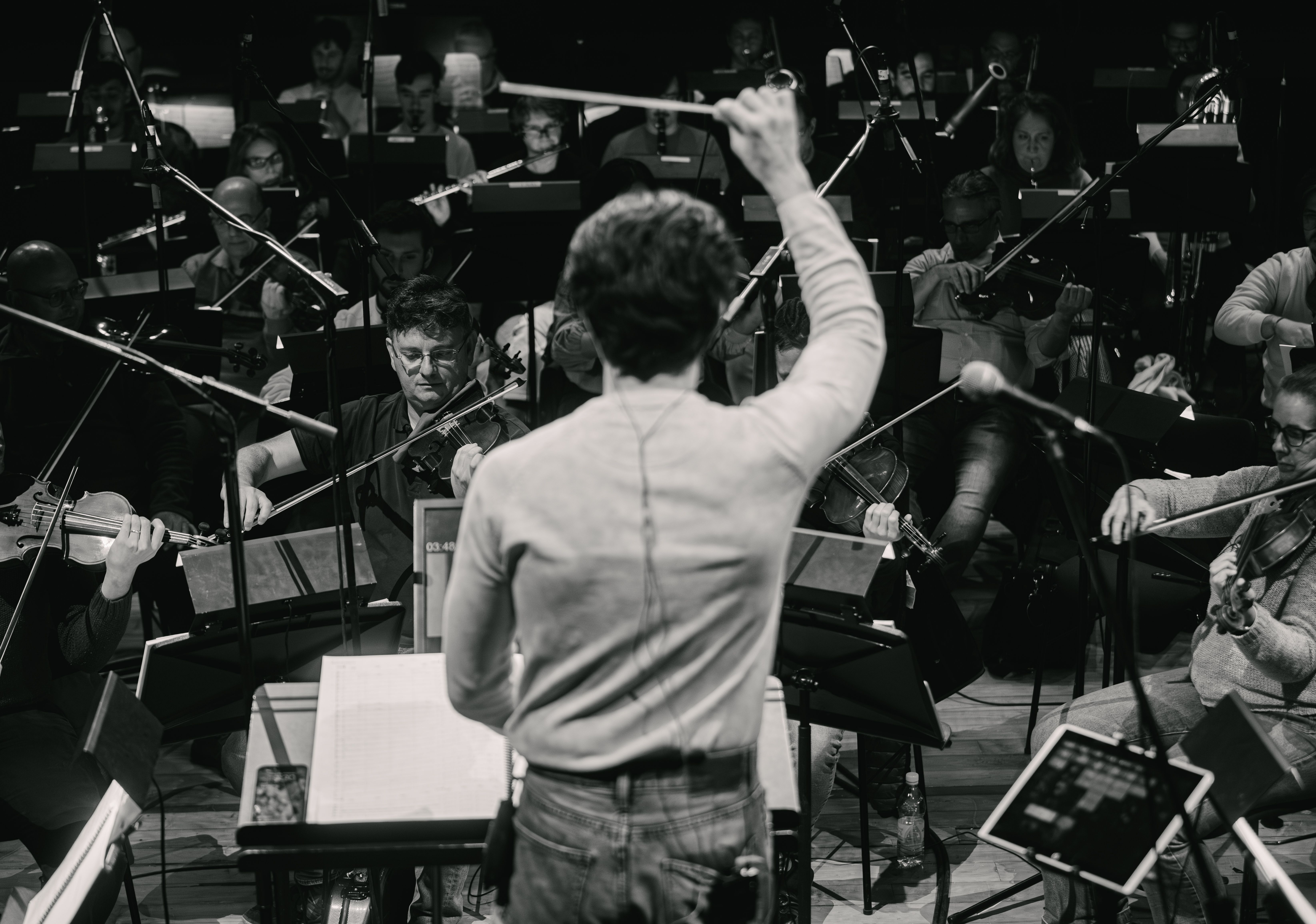 A conductor with his back to the camera conducts an orchestra