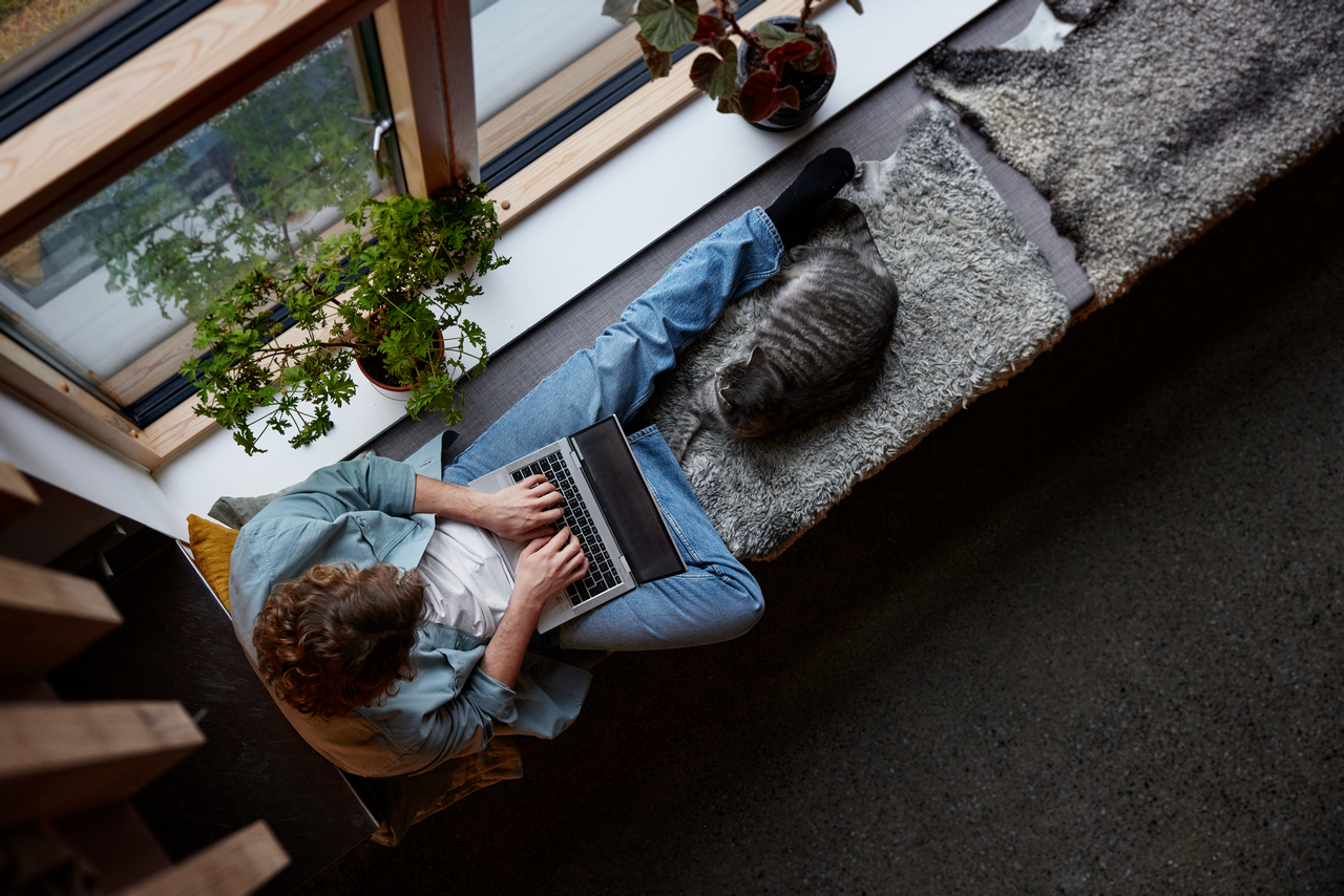 A guy with laptop on his lap, sitting on windowsill.