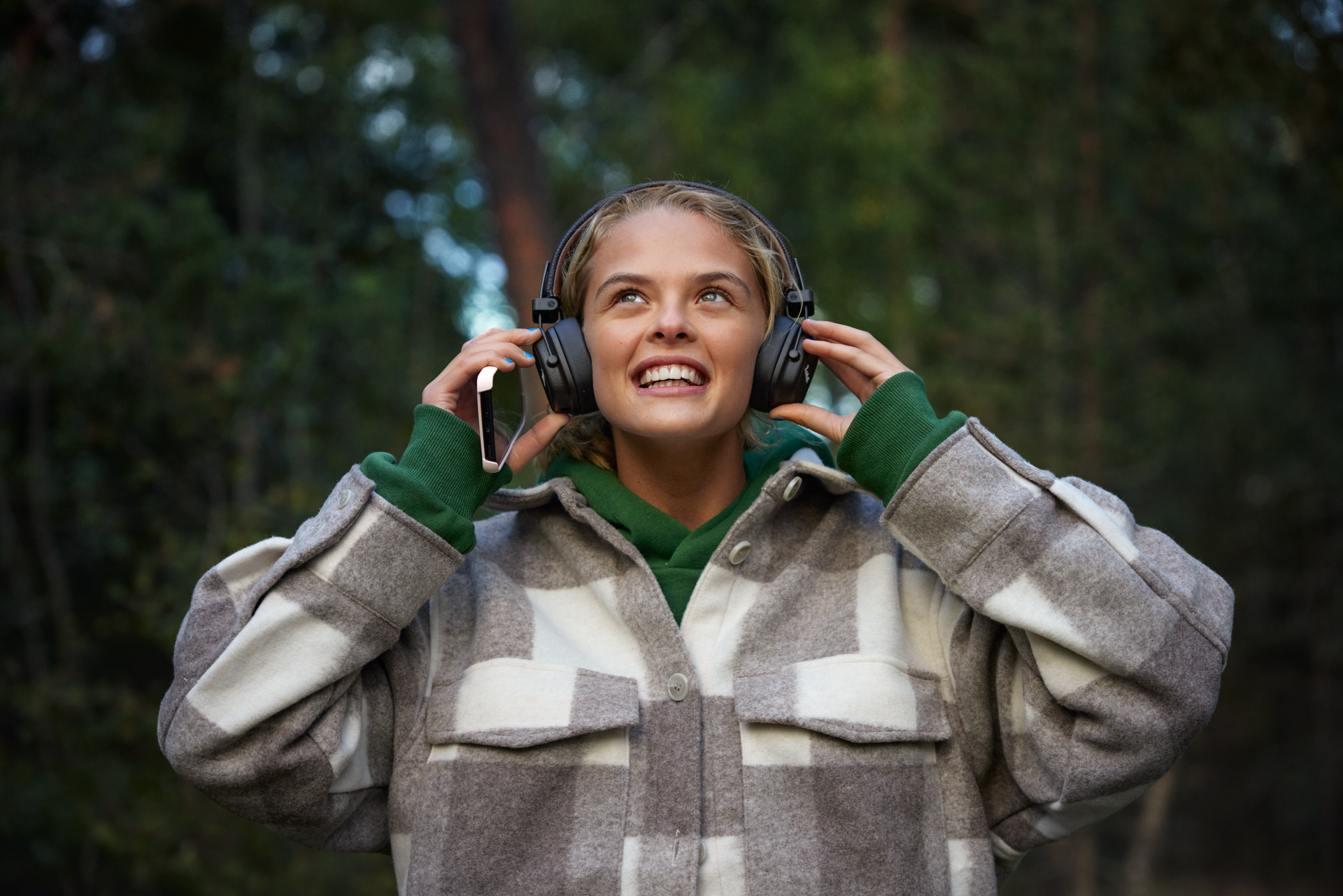 Glad jente med over-ear-hodetelefoner, holder en mobil.