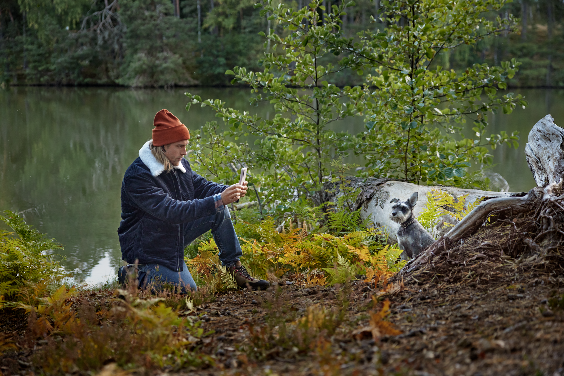 Mies metsässä ottaa kuvaa koirastaan puhelimella.