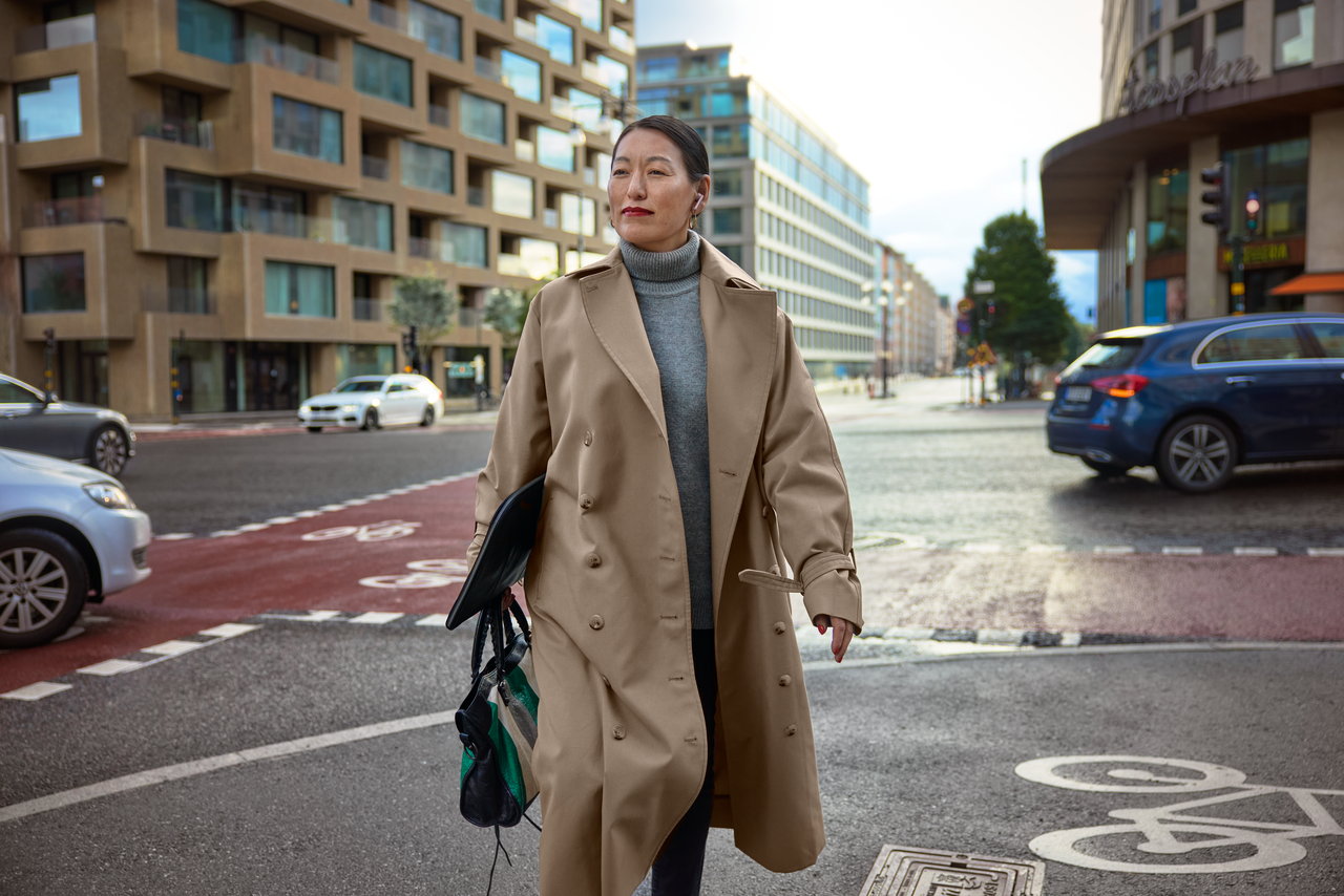 A woman in business attire is walking in the city with wireless earbuds and a laptop.