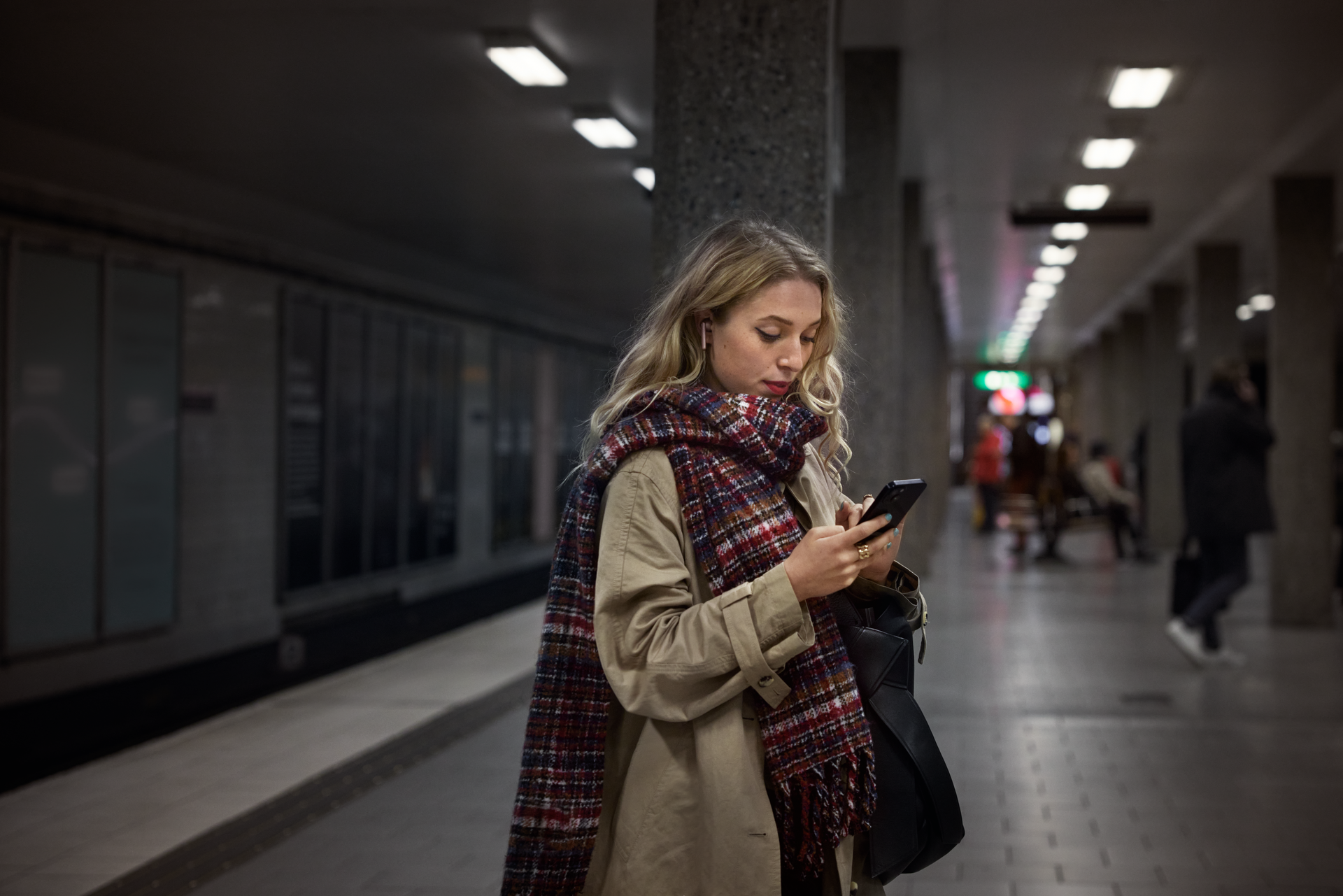 Nainen seisoo metroasemalla ja katsoo puhelintaan.