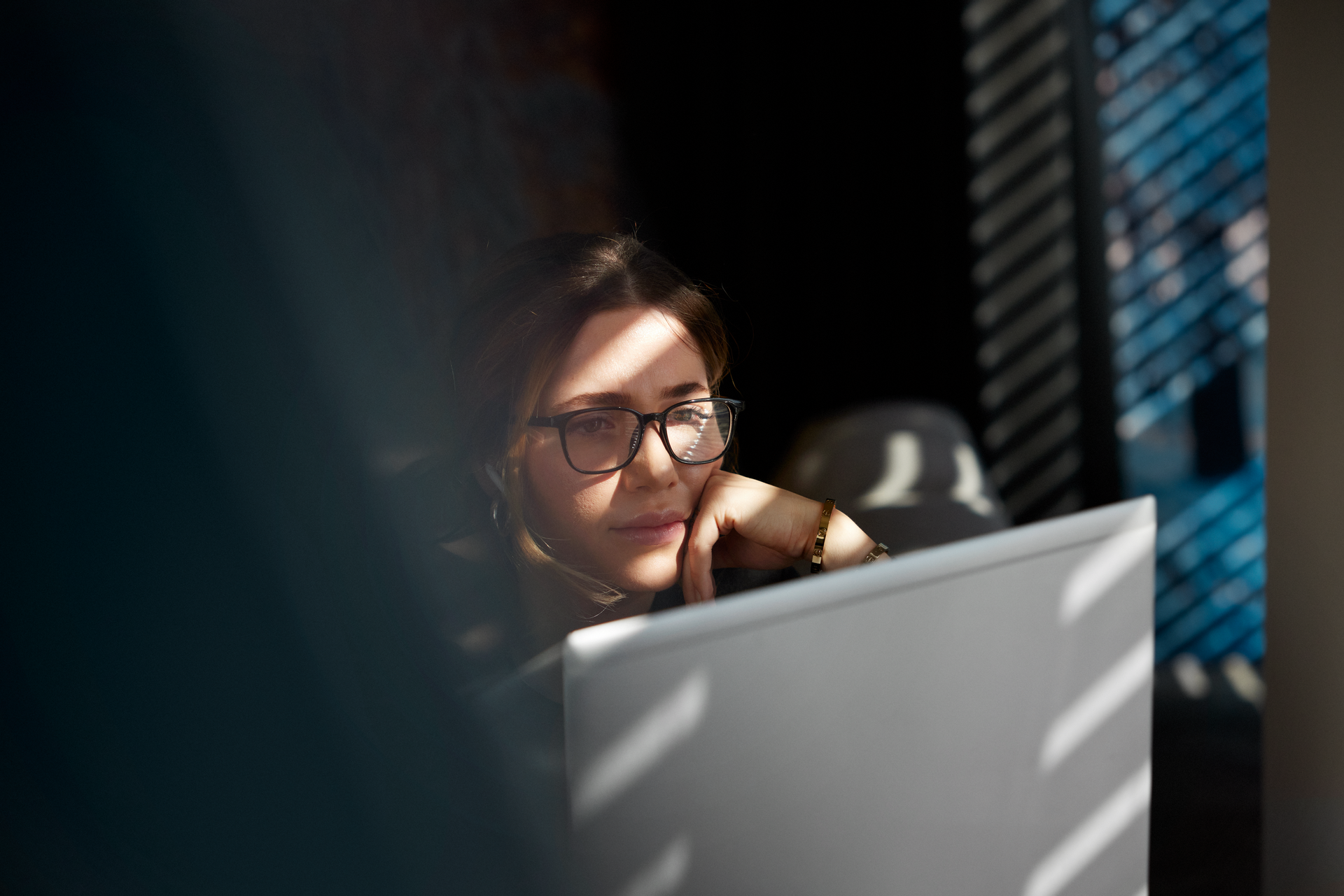 A woman wearing glasses, looking at a computer screen.