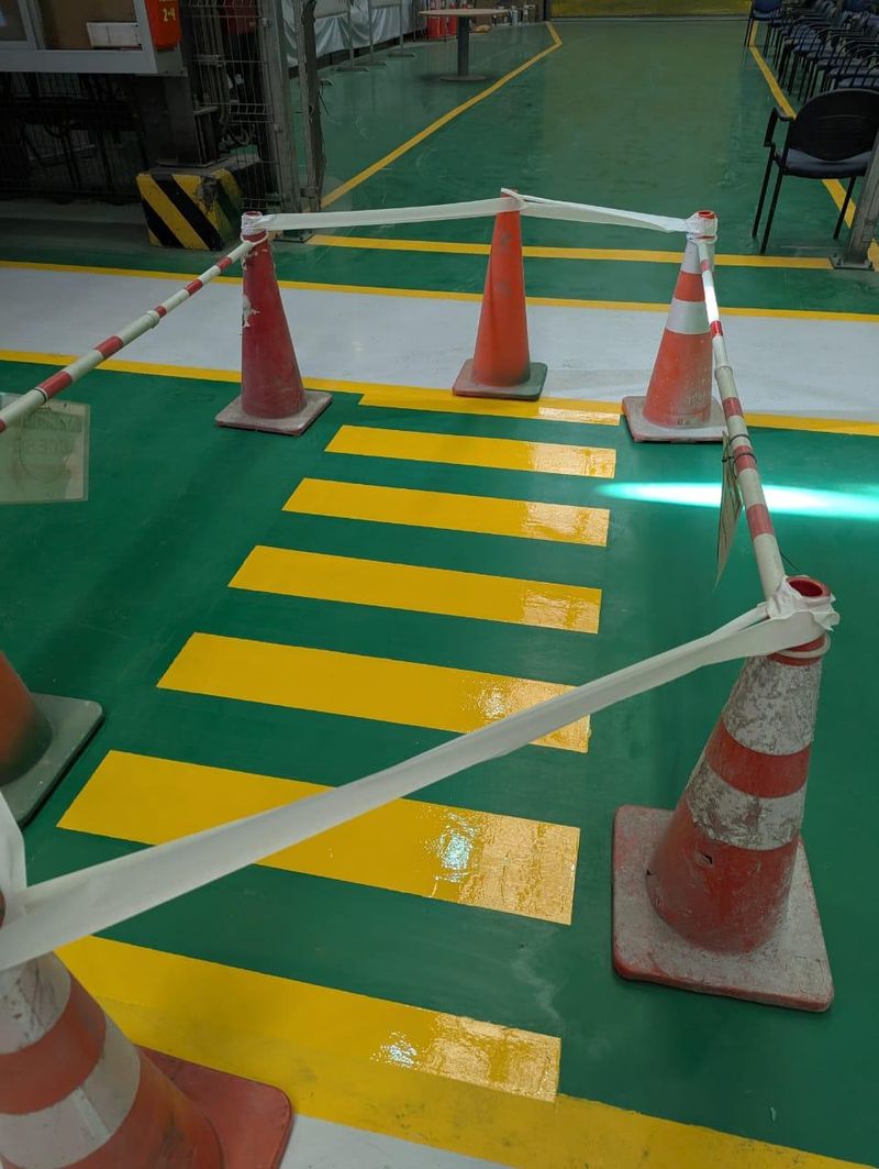 Piso industrial revestido, con señalización de cruce peatonal en amarillo sobre fondo verde
