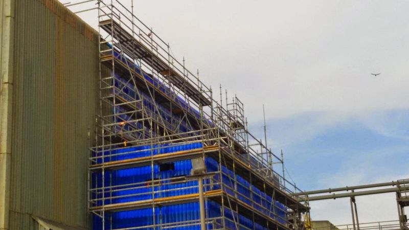 Andamiaje modular instalado en fachada de estructura industrial revestida en azul