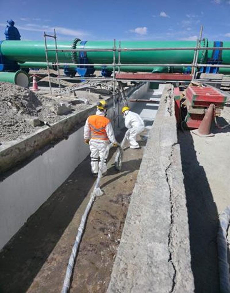 Trabajadores aplicando revestimiento sobre canal de hormigón junto a tuberías de proceso