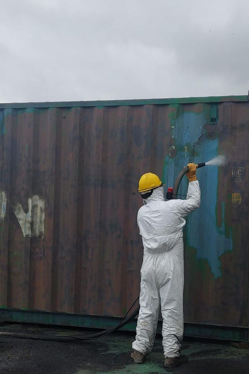 Trabajador aplicando granallado ecológico sobre contenedor metálico