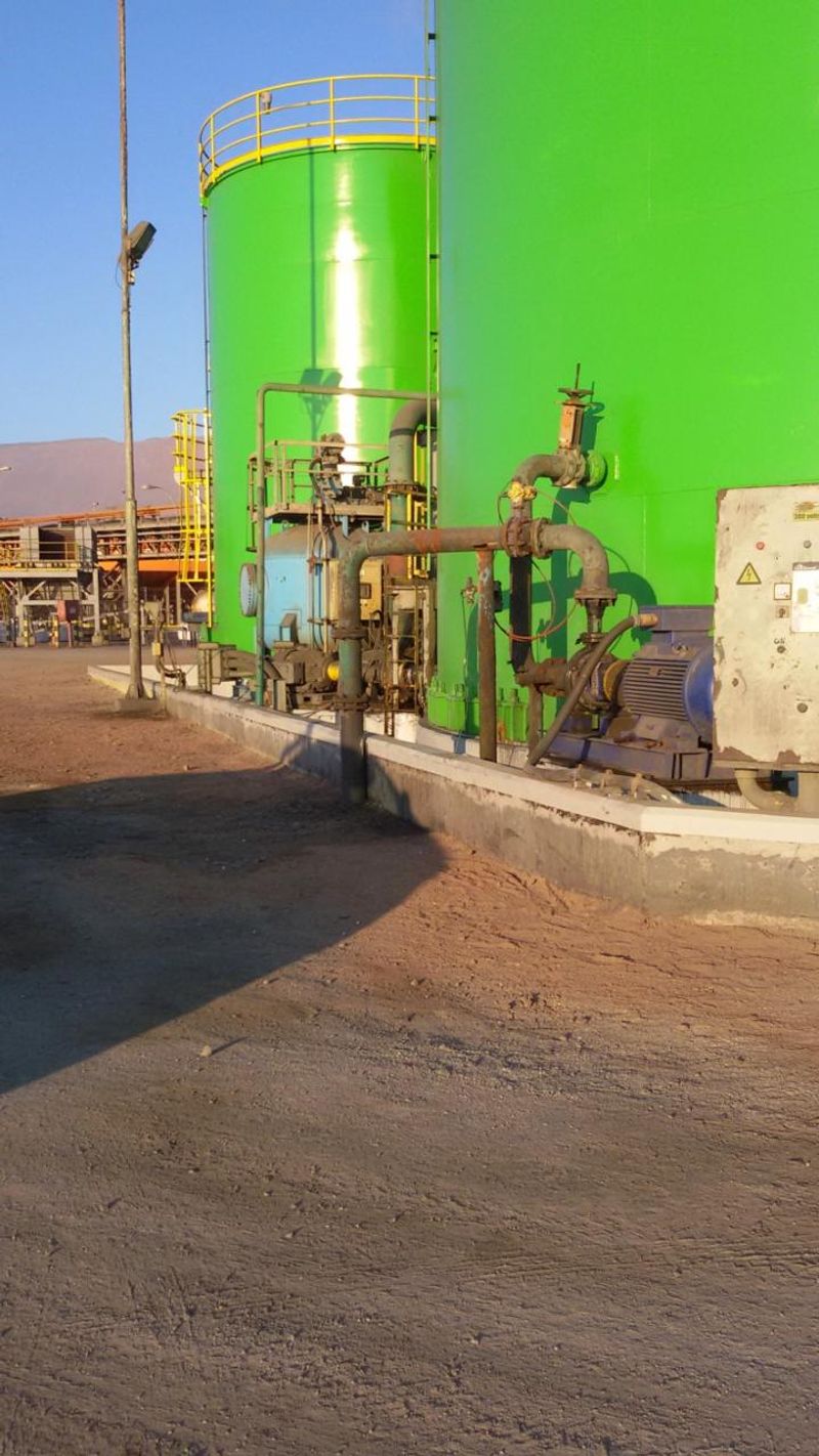 Estanques industriales revestidos en verde, con equipos de bombeo en primer plano