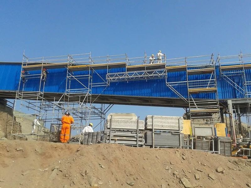 Andamio modular tipo pasarela entre estructuras industriales, con trabajadores en altura