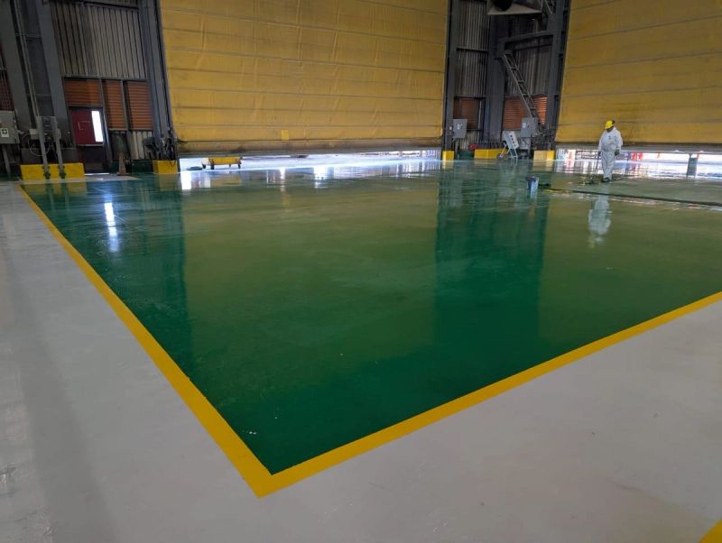 Aplicación de revestimiento epóxico verde en piso industrial, con trabajador en terreno