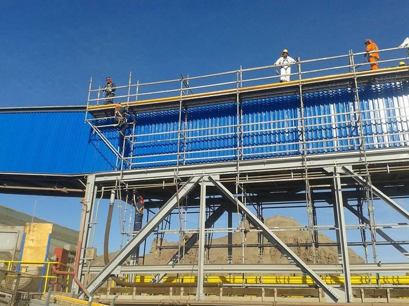 Trabajadores en plataforma de andamio modular a gran altura, con vista a faena minera