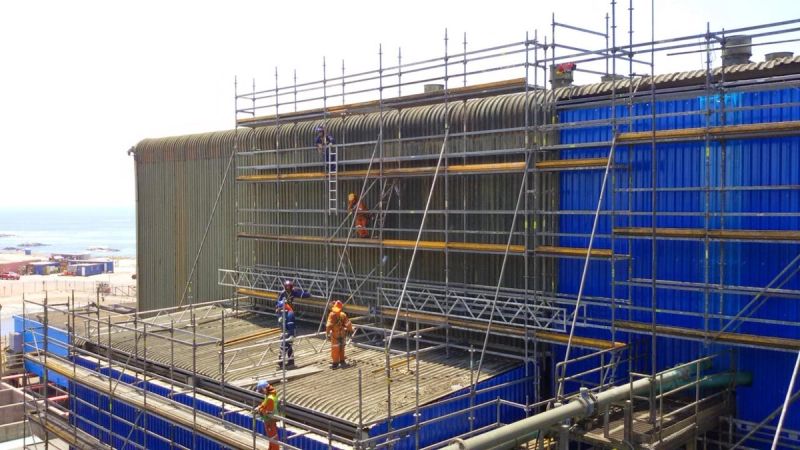 Vista interior de una torre de andamio modular de gran altura, con trabajadores en la parte superior