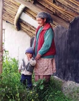 Woman standing with a child beside a vegetable garden outside a traditional Himalayan home.