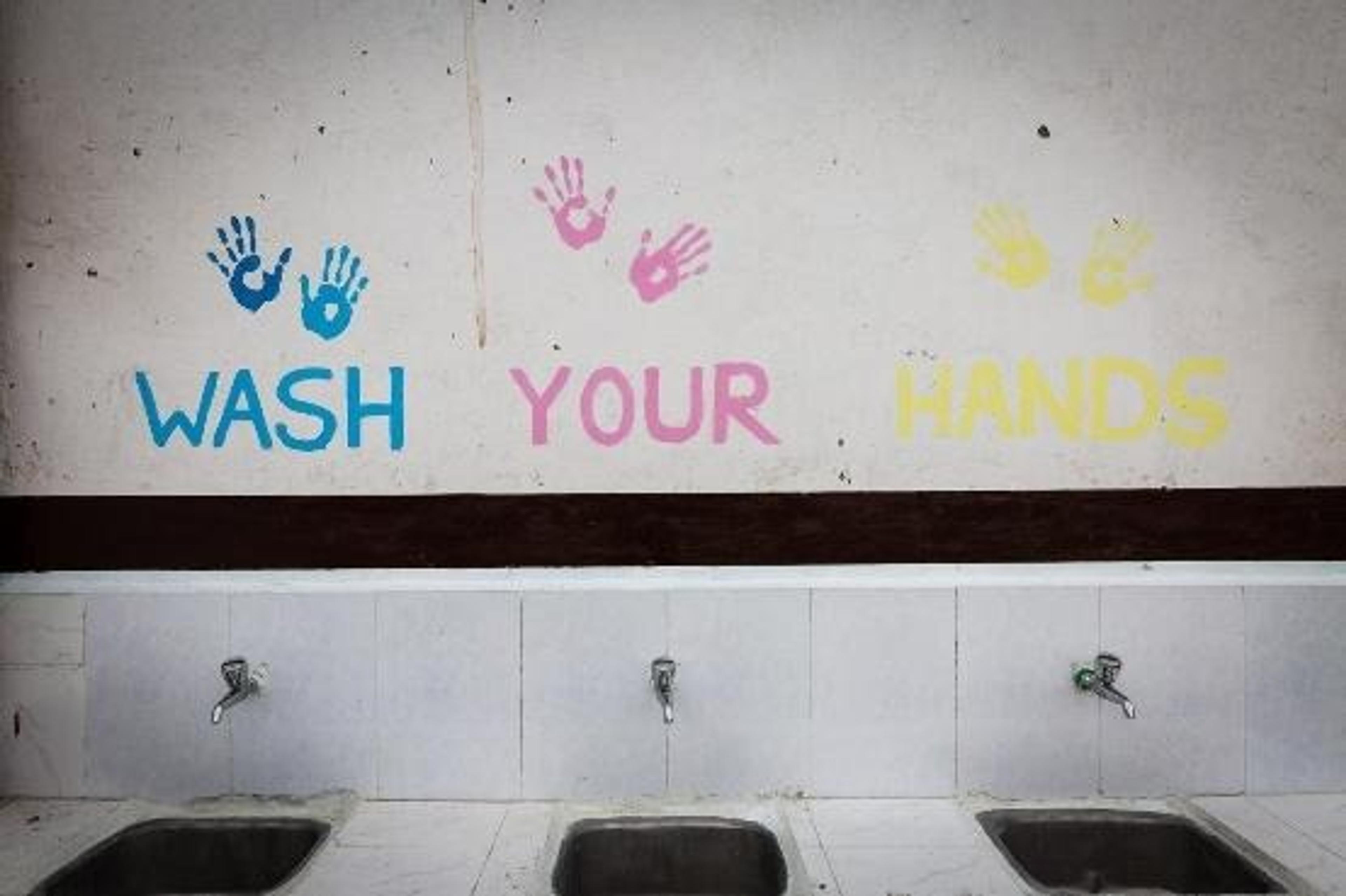 Three handwashing sinks beneath a colorful “Wash Your Hands” sign with painted handprints.