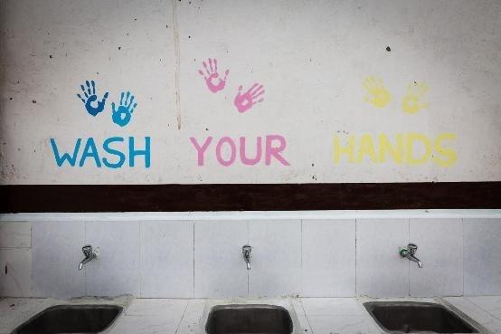 Three handwashing sinks beneath a colorful “Wash Your Hands” sign with painted handprints.