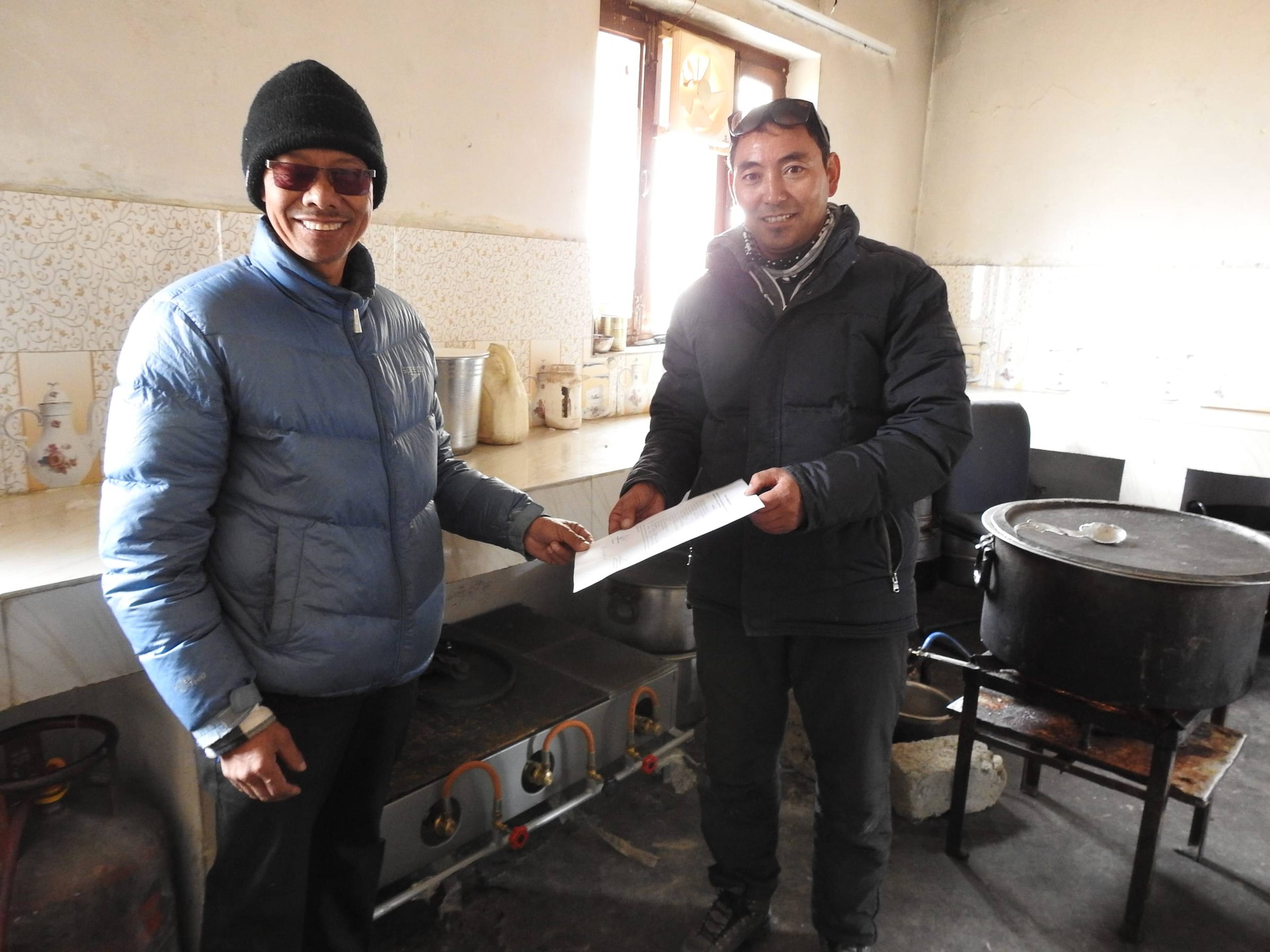 A LEHO representative hands over kitchen equipment documentation to the Puga hostel principal, part of ongoing support for local school infrastructure.
