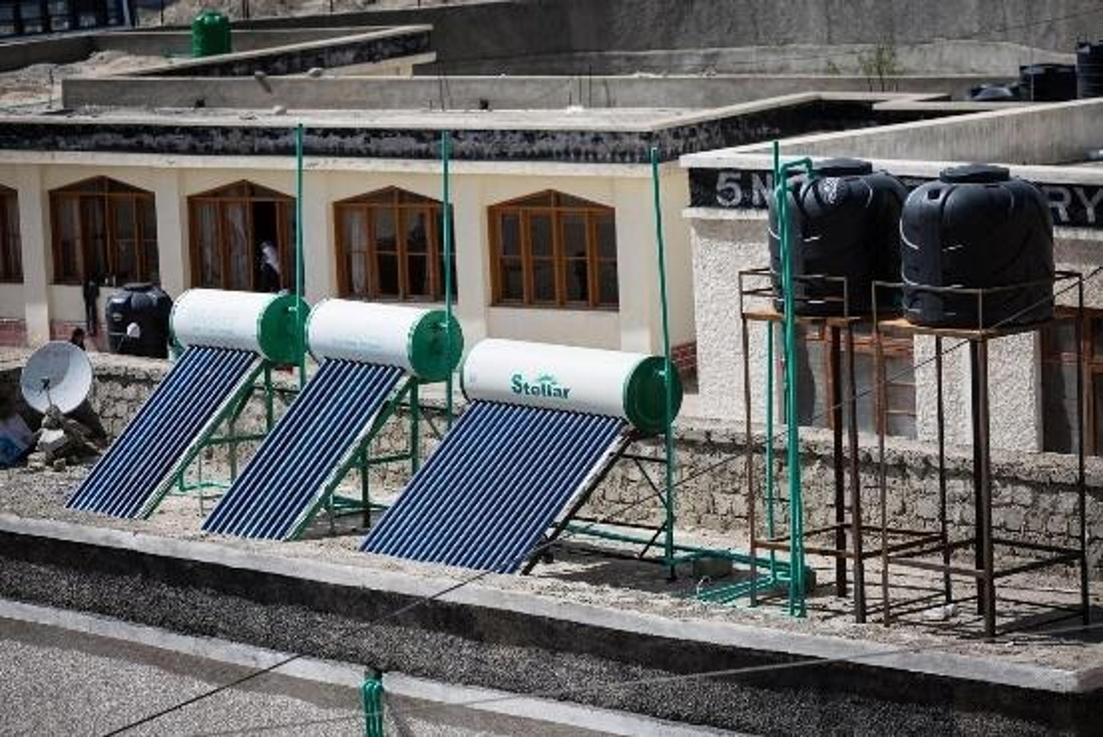 Solar water heating system with three solar thermal collectors and insulated water storage tanks installed on the roof of a school building.