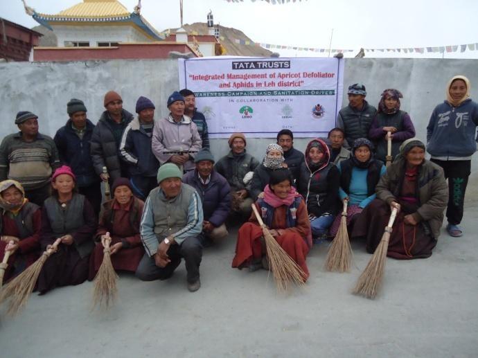 Group of community members holding traditional brooms during an apricot orchard sanitation and pest-control campaign supported by Tata Trusts and local partner organizations.
