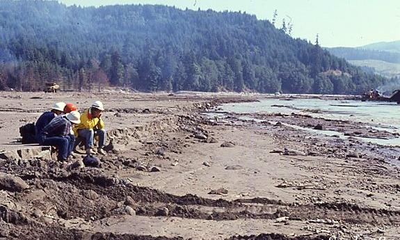 People in hard hats survey sit to the damage of the May 1980 eruption of Mount St. Helens in August 1980.