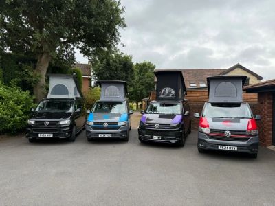 Four T.C. Campers VW campervans parked in a row with their pop-top roofs raised