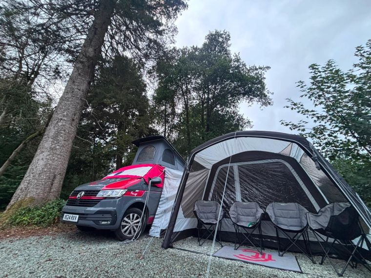 A VW campervan parked in the woods with awning attached to the campervan