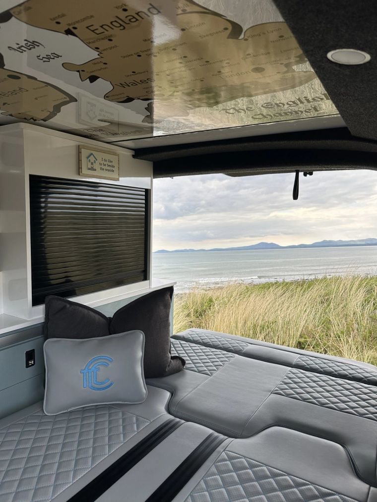 A VW campervan parked above a calm sea loch in soft evening light