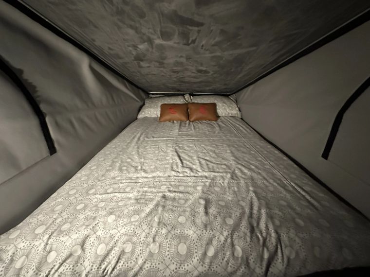 A double bed made up in the pop-top roof, with patterned bedding and branded cushions