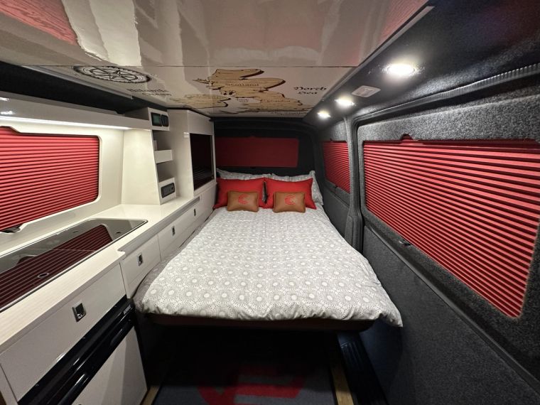 Fenyx with the bed made up, red blackout blinds down and the kitchen alongside