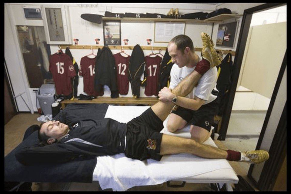 Footballer receiving assisted stretching from a physiotherapist in a club treatment room, illustrating the growing role of recovery and injury management in modern football.