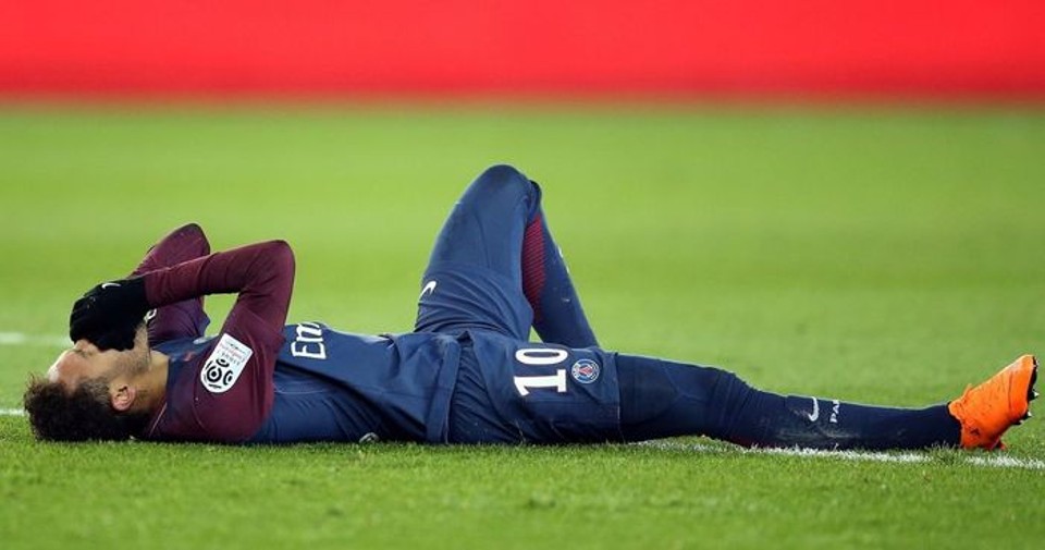 Professional footballer Neymar lies on the pitch holding his face after an injury during a match, highlighting the physical setbacks that can interrupt even the careers of elite players.