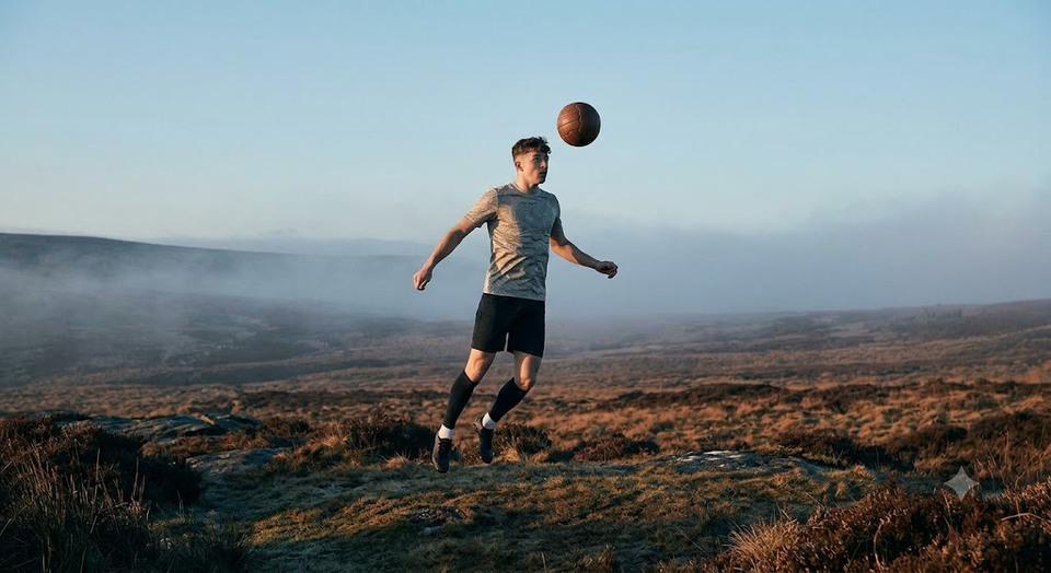 Young athlete balancing a football in a natural outdoor landscape, representing the connection between nature, movement, and athletic development explored in this article.