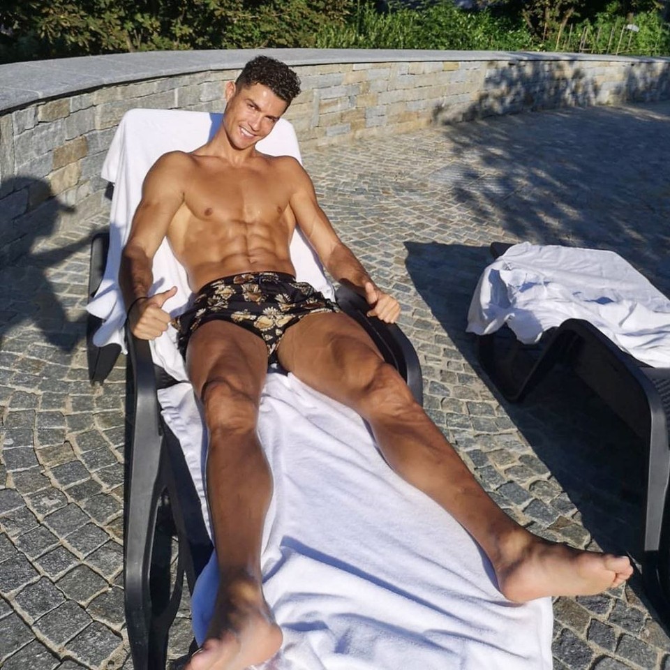 Cristiano Ronaldo relaxing shirtless on a sun lounger outdoors, giving a thumbs-up while recovering in the sun.