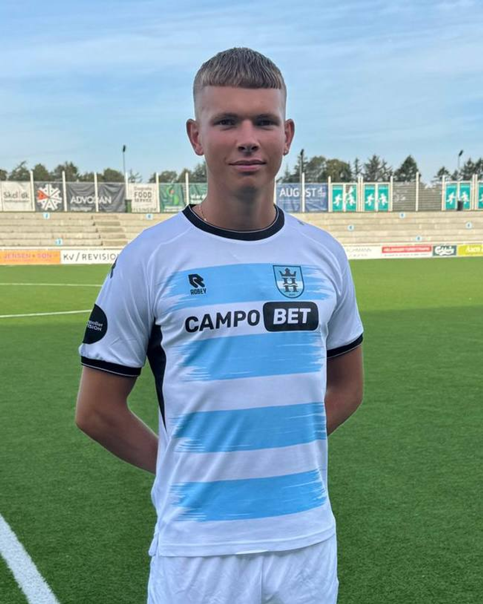 Professional footballer Frederik Vestergaard Kristensen stands on the pitch wearing his new club's white and light blue home kit after signing, posing for an official team .