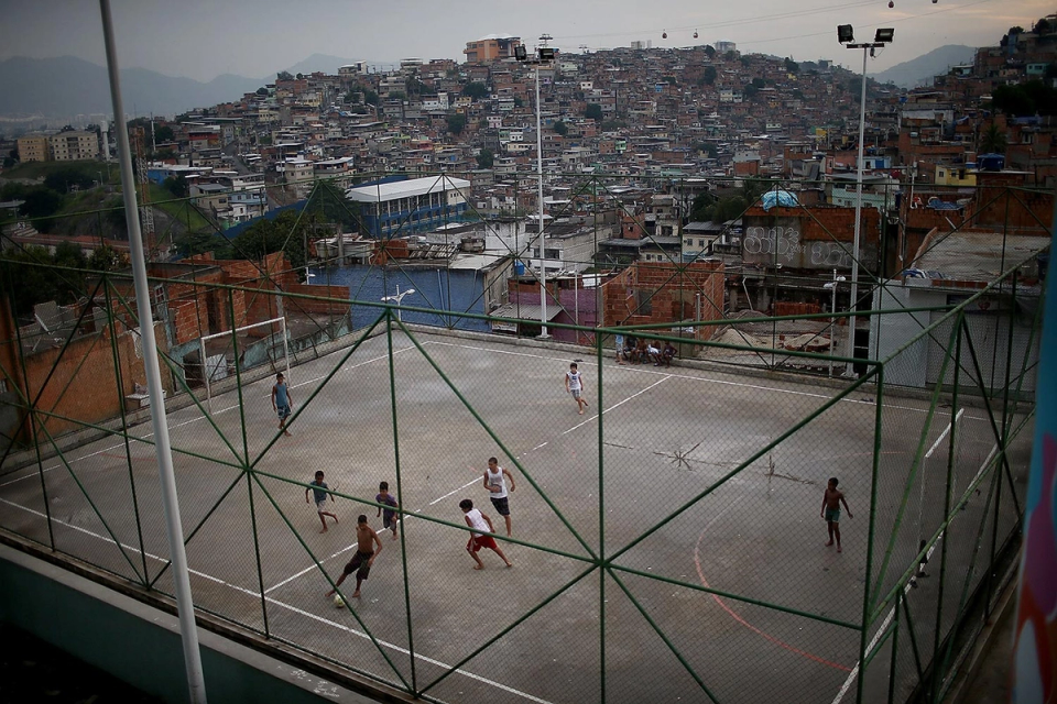 Children playing small-sided football on a concrete court overlooking a densely populated neighborhood, illustrating the street football environments that naturally develop creativity and skill.