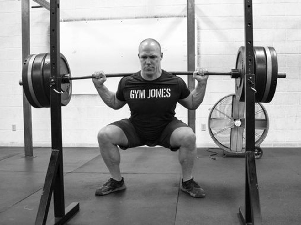 Athlete performing a heavy barbell back squat inside a power rack with multiple weight plates, illustrating traditional maximal strength training commonly used in athletic conditioning.