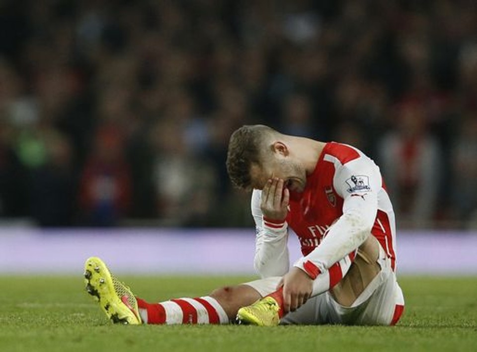 Professional footballer Jack Wilshere sits on the pitch holding his face after suffering an injury during a match, illustrating how recurring injuries can derail the career of even the most promising young talent.