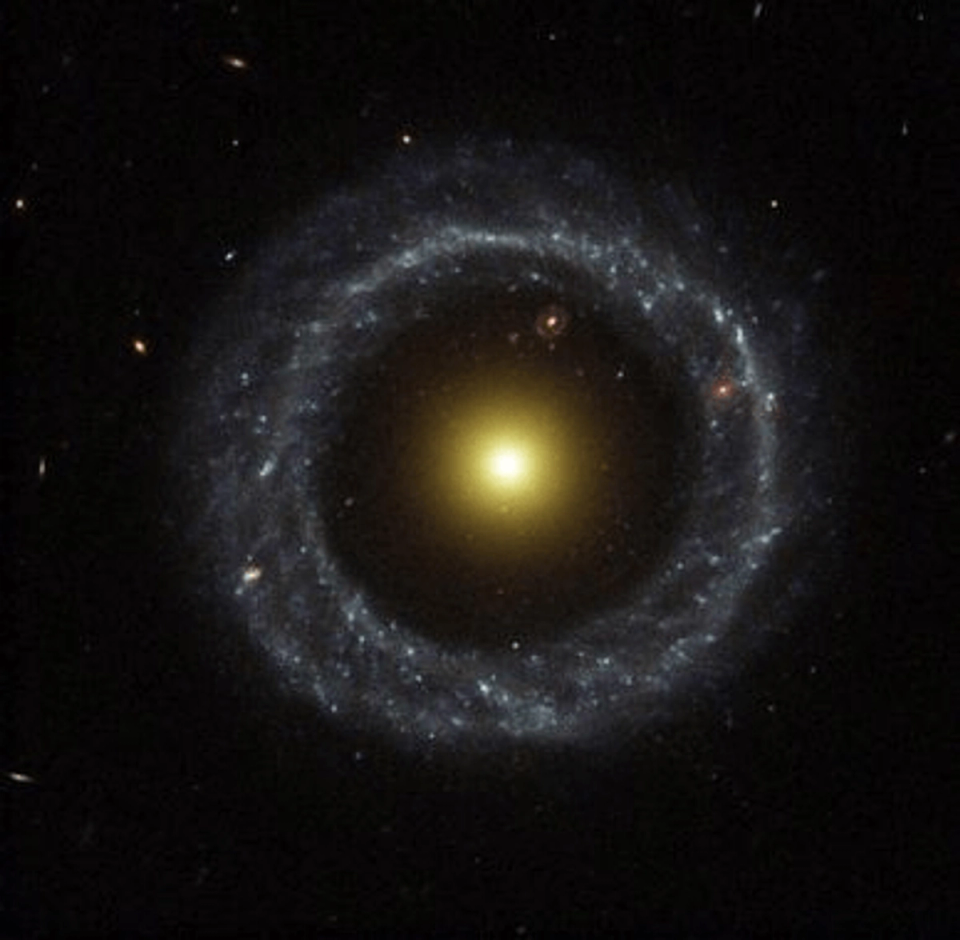 Astronomical a ring galaxy with a bright yellow core surrounded by a glowing circular band of stars against the darkness of space.