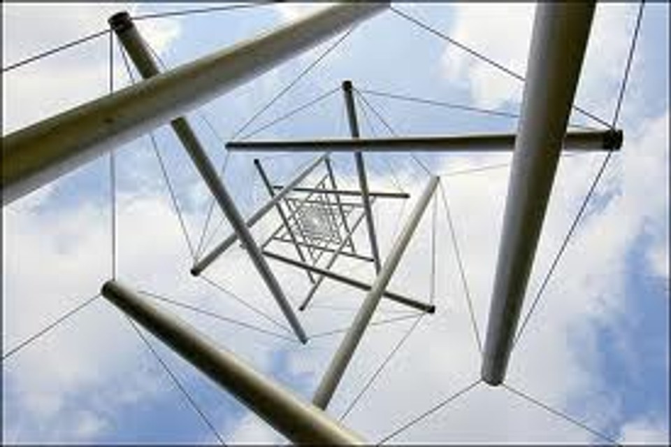 View looking upward through a tensegrity sculpture made of suspended rods and tension cables, illustrating how stability emerges from balanced forces across an interconnected structure rather than rigid support alone.