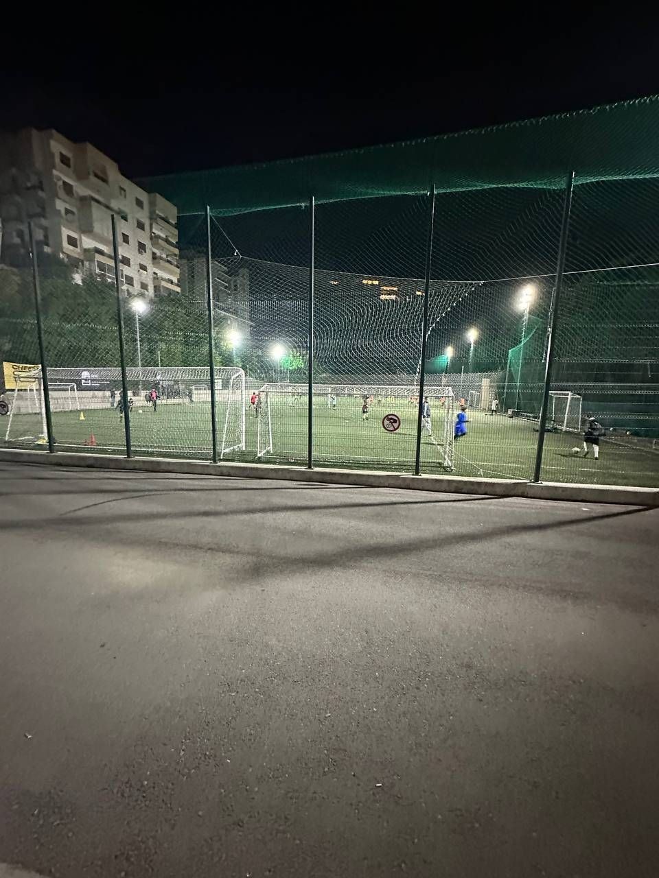 Nighttime view of a floodlit football pitch in Lebanon with players training during a small-sided match, reflecting Taylor Davidson's return to consistent football throughout 2025.