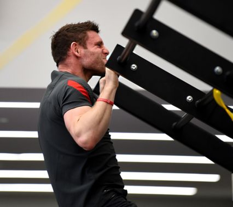 A man performs a pull-up on a gym rig with a strained facial expression, illustrating an upper-body strength exercise focused on pulling power and muscular endurance.