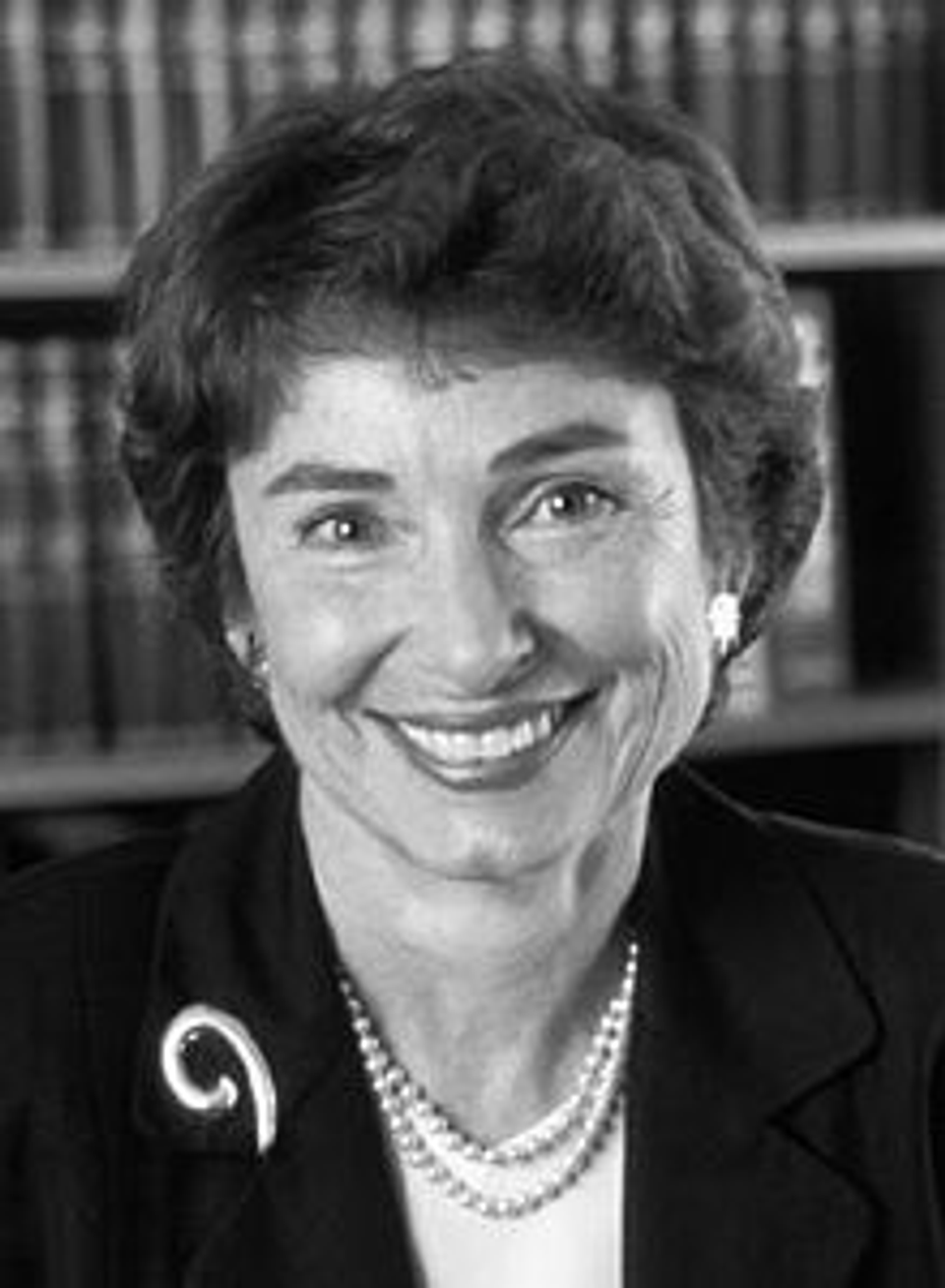 Black-and-white portrait of a smiling female scientist and academic in formal attire, photographed in front of bookshelves.
