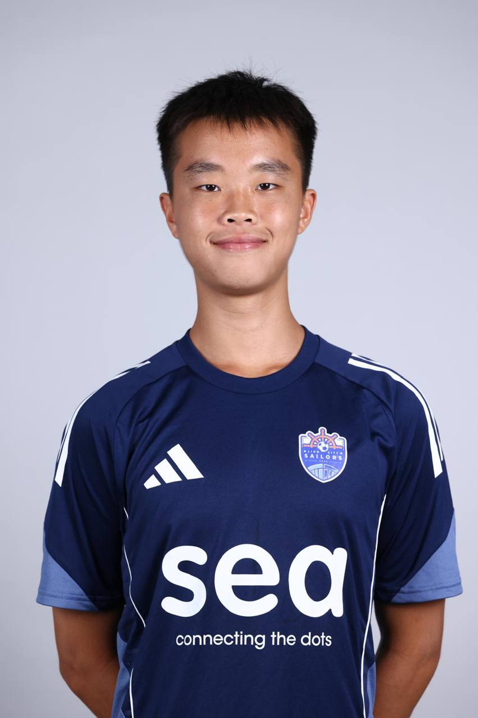 Professional footballer Ryan Lim poses in his official navy blue Lion City Sailors kit during club media day, standing against a neutral background for his team portrait.
