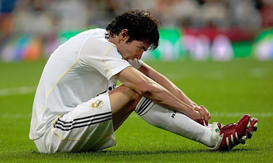 Professional footballer Kaká sits on the pitch clutching his lower leg in pain after an injury, illustrating how injuries can affect performance and longevity at the highest level of football.