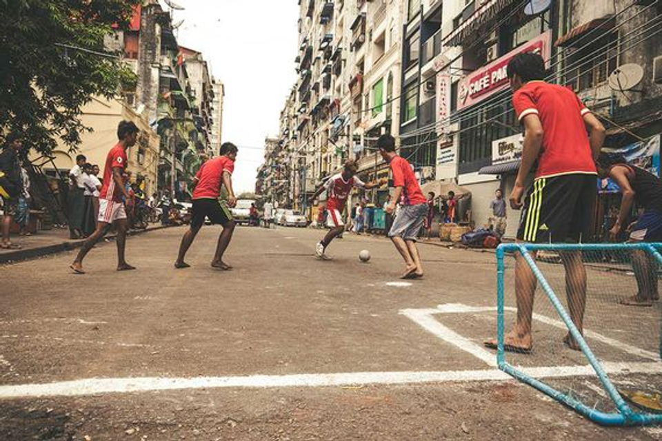Children playing street football in an urban neighborhood, illustrating the unstructured free play and creativity that help develop world-class footballers.