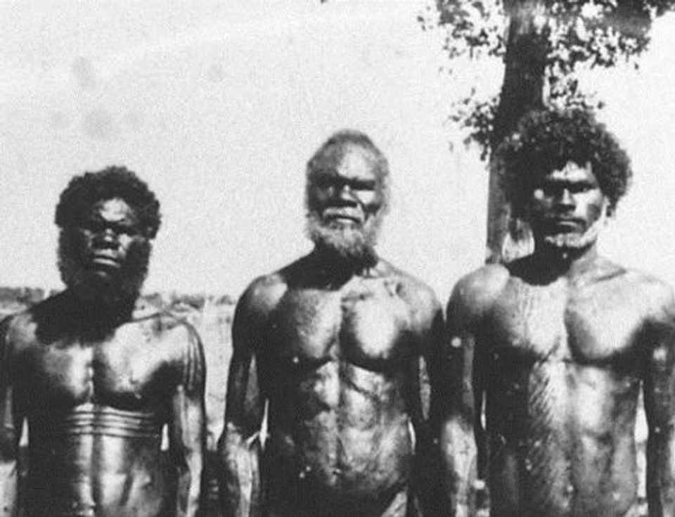 Black-and-white photograph of three Indigenous Australian men with lean, muscular physiques standing outdoors, illustrating natural athletic development through an active lifestyle.
