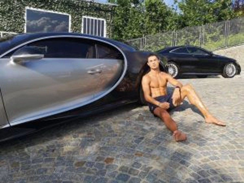 Cristiano Ronaldo sitting barefoot on the ground beside a sports car outdoors, relaxing in the sun after training.
