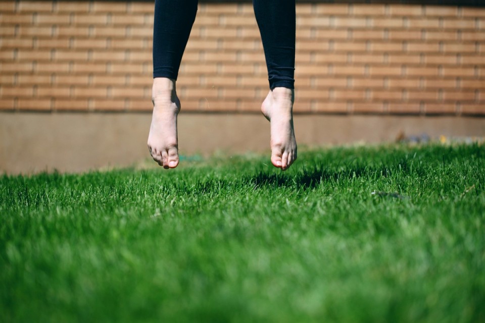 Bare feet hovering above natural grass, representing the connection between the human body, natural movement, and the outdoor environment discussed in this article.